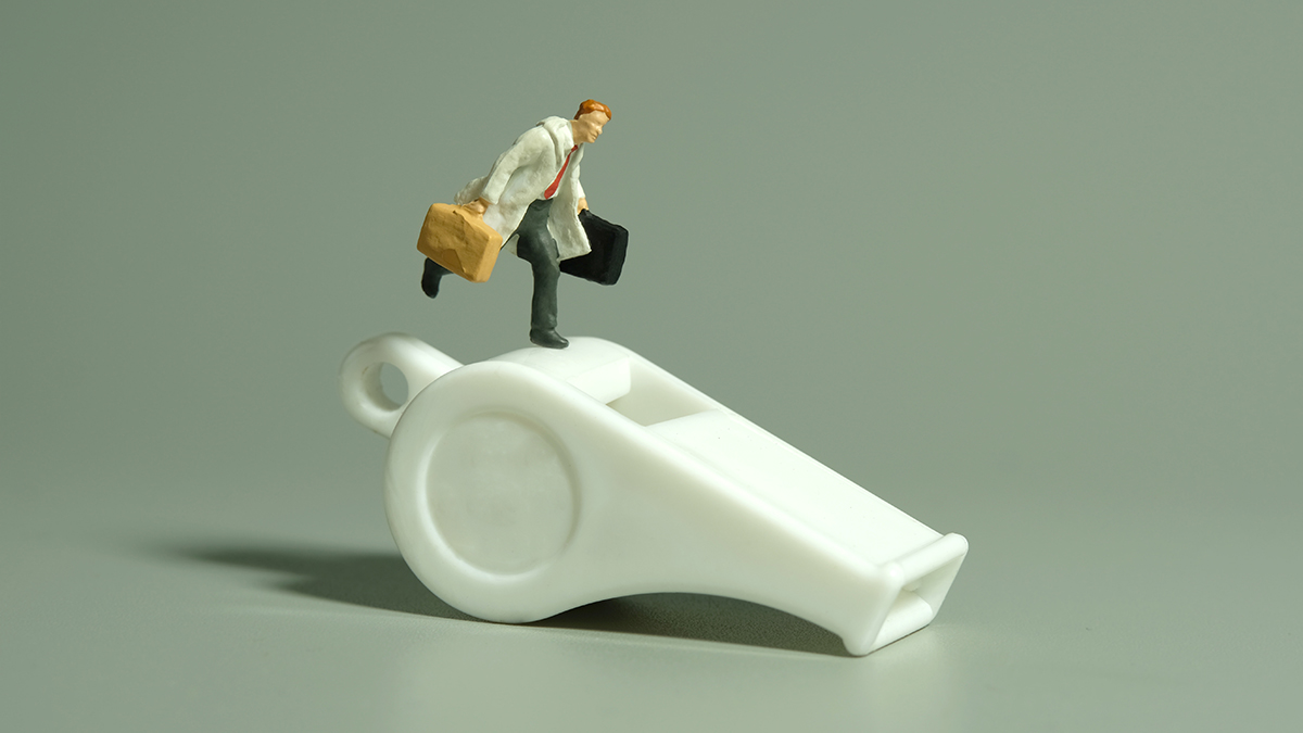 Miniature people toy figure photography. Whistle blower concept illustration. A businessman running above white whistle, isolated on grey background.