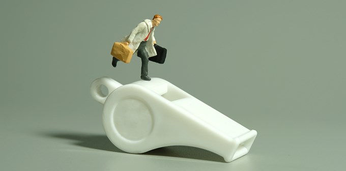 Miniature people toy figure photography. Whistle blower concept illustration. A businessman running above white whistle, isolated on grey background.