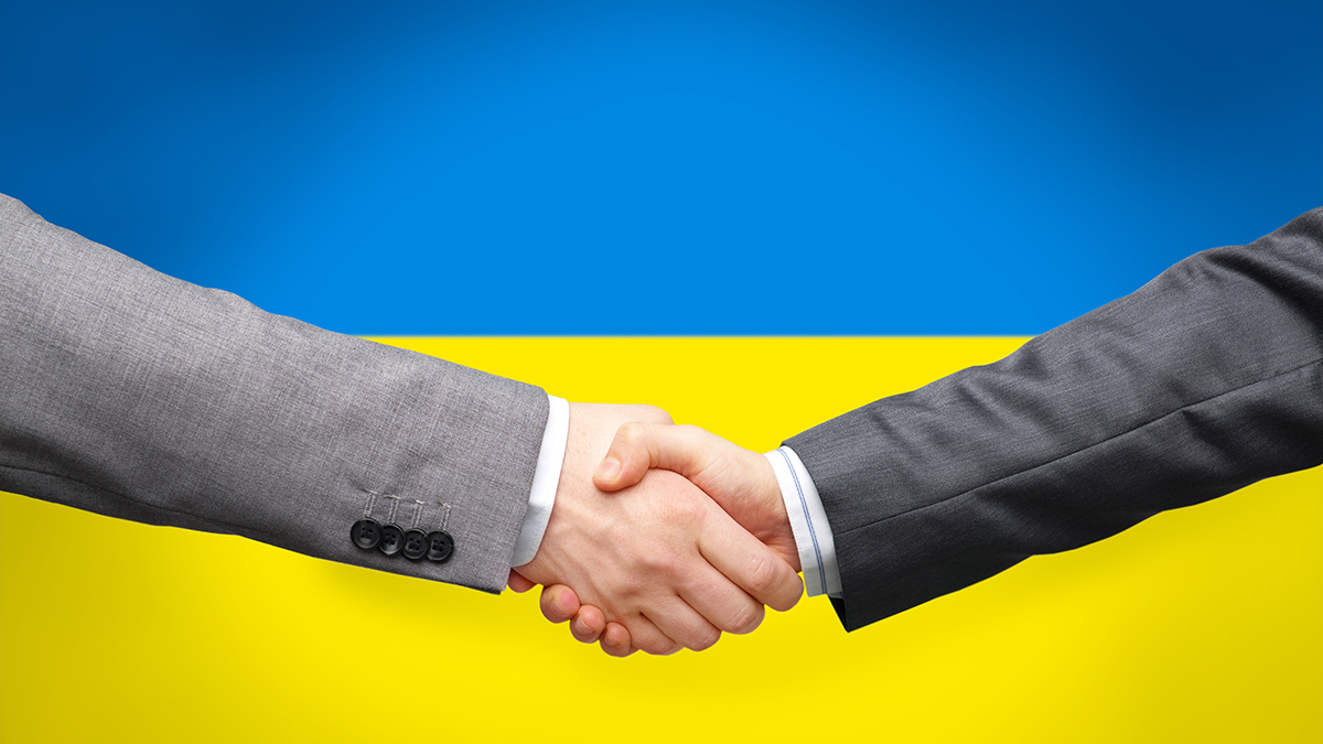political, business and national concept - close up of handshake over colors of flag of ukraine on background