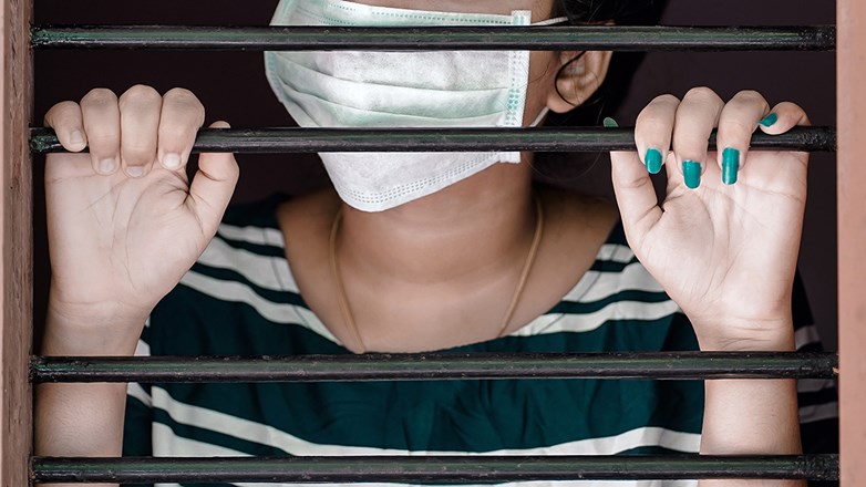 Girl behind bars with a facemask covering her mouth.