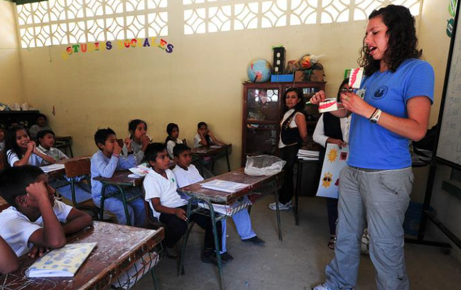 Children sitting at desks and a person teaching