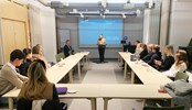 Several students sitting around a u-shaped desk looking towards and listening to a presenter up front. A powepoint slide is projected with a text "thank you for listening" and a with a Svensk Handel logo on it.