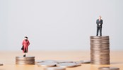 Miniature figure of businessman standing on higher than coins stacking of businesswoman for inequality of gender male and female of income and salary concept.