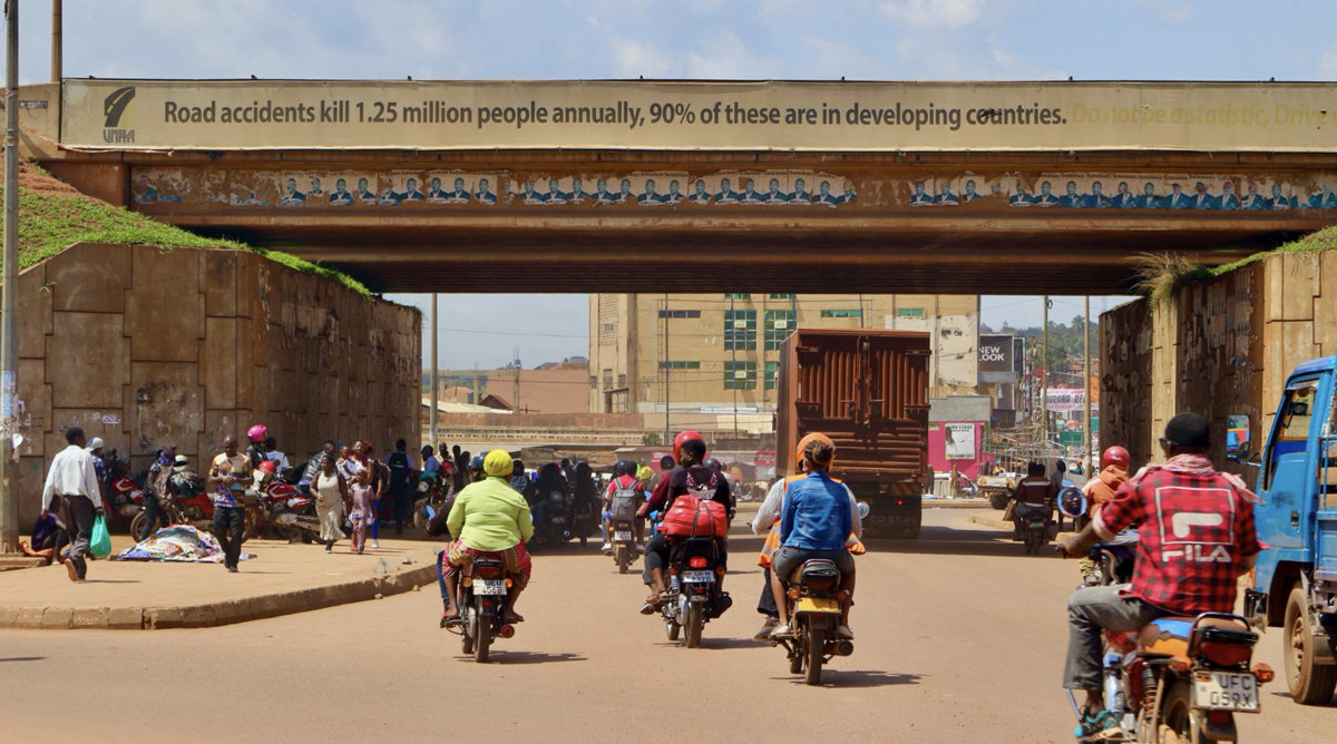 Traffic on a sandy road in Africa. Pedestrians walk among mopeders and trucks driving under a viaduct.