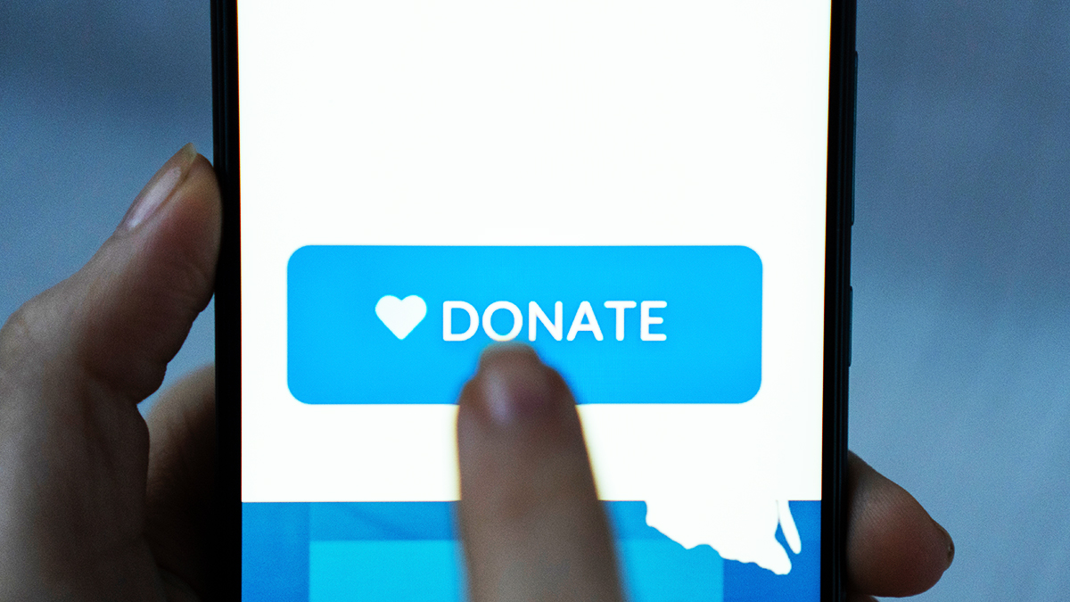 Close-up finger pressing donate icon button on blue screen on black mobile phone.