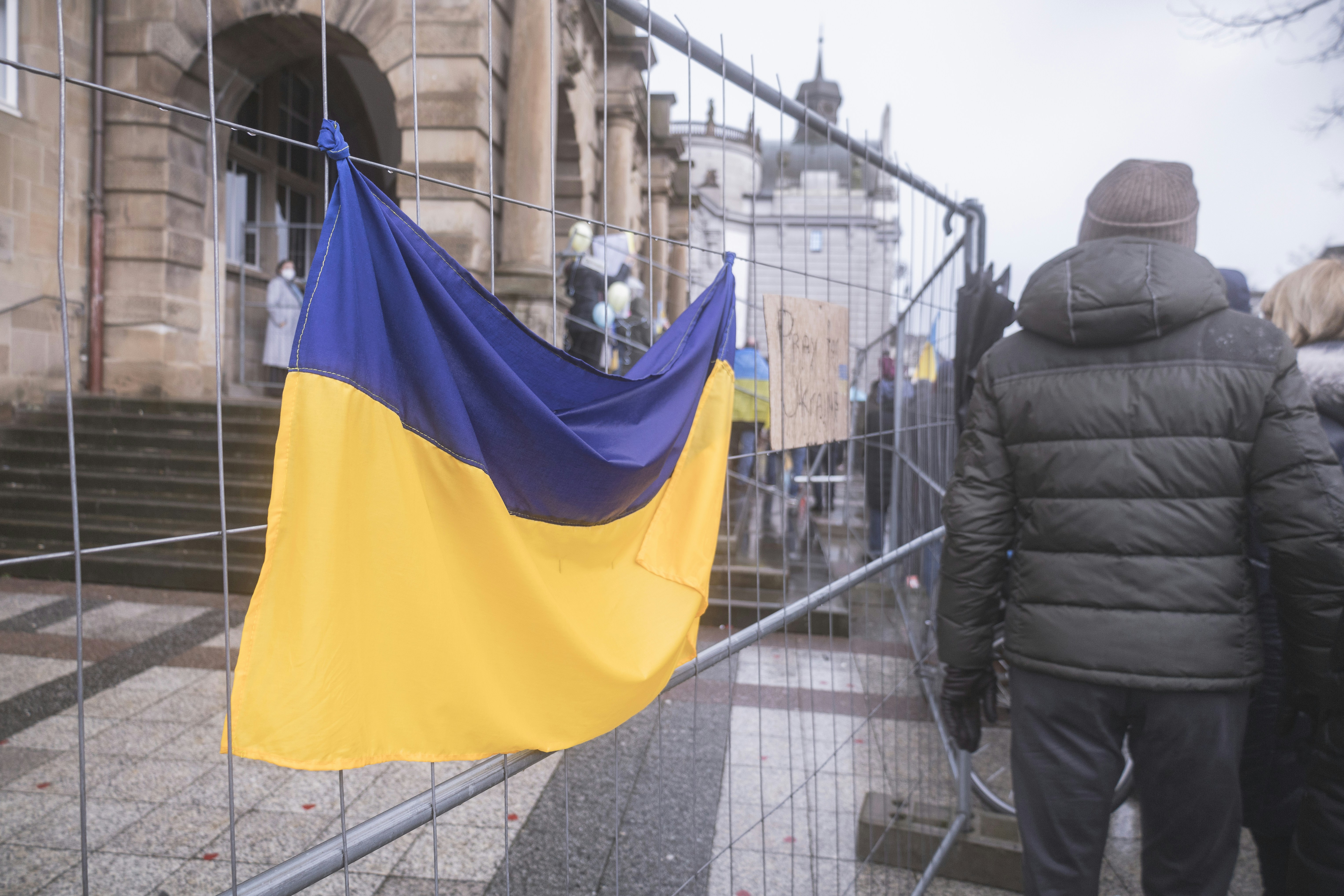 Ukrainian flag mounted on construction bars with people walking past it.