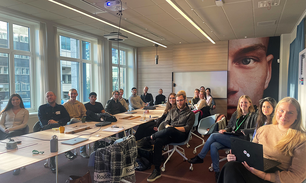 Group of students and company reps from Coop sitting around a conferene table smiling and looking into the camera