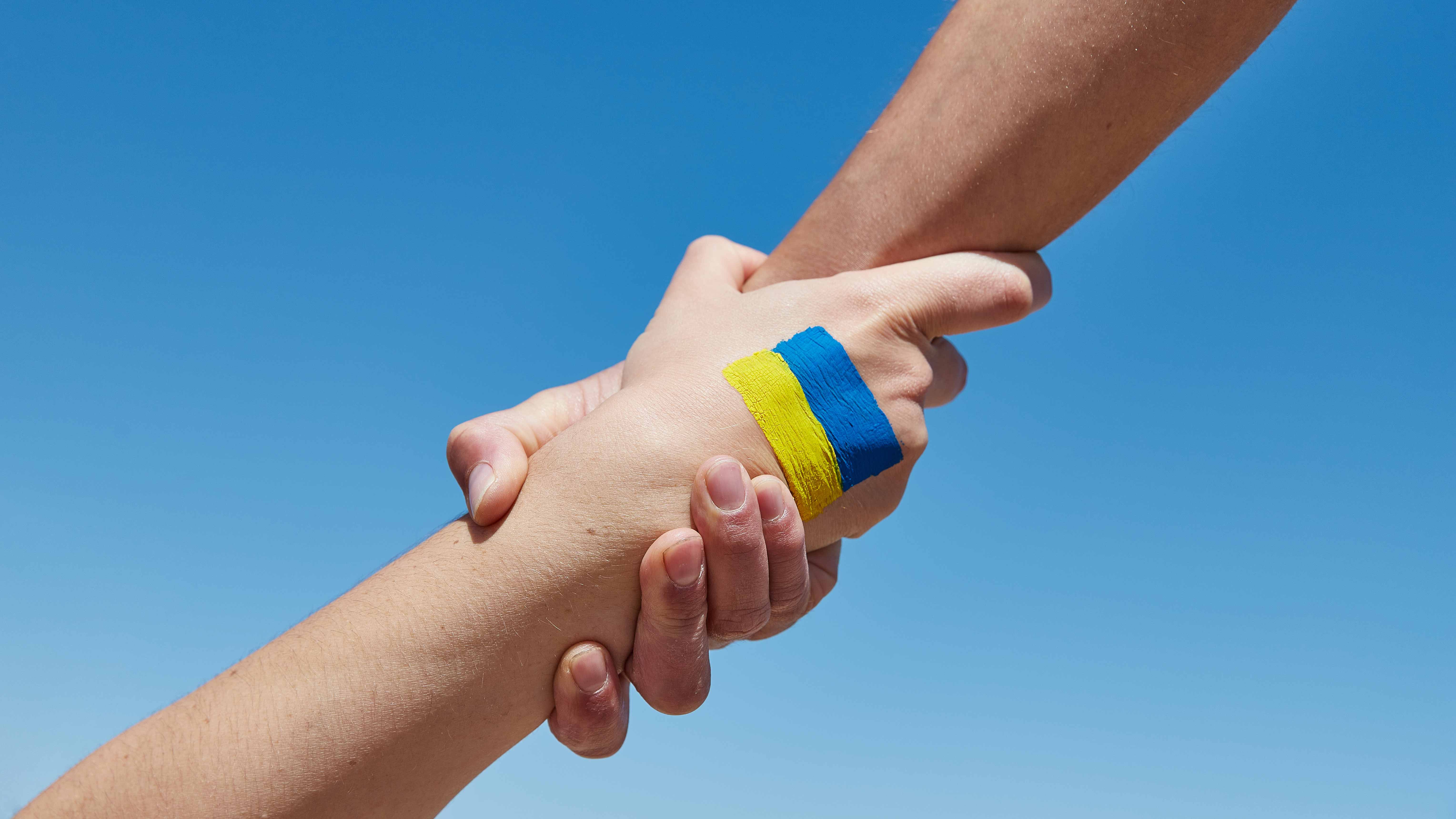 Lend a hand help painted in ukrainian flag colors against blue sky. Stand with Ukraine