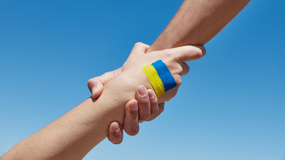 Lend a hand help painted in ukrainian flag colors against blue sky. Stand with Ukraine.