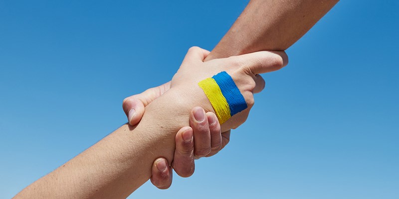 Lend a hand help painted in ukrainian flag colors against blue sky. Stand with Ukraine.