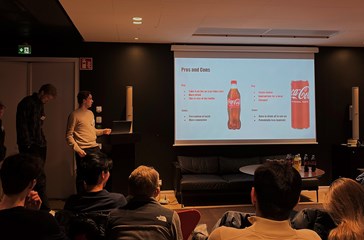 A student presenting in fron of a coca-cola labelled ppt in a dark lit room.