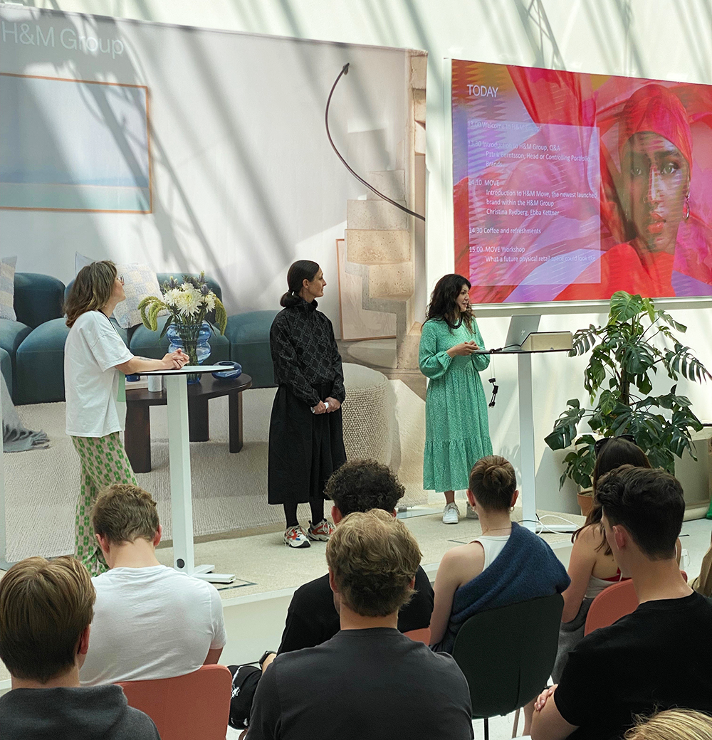 Three representatives from H&M holding a precentation in fron of students in a lit up atrium room.