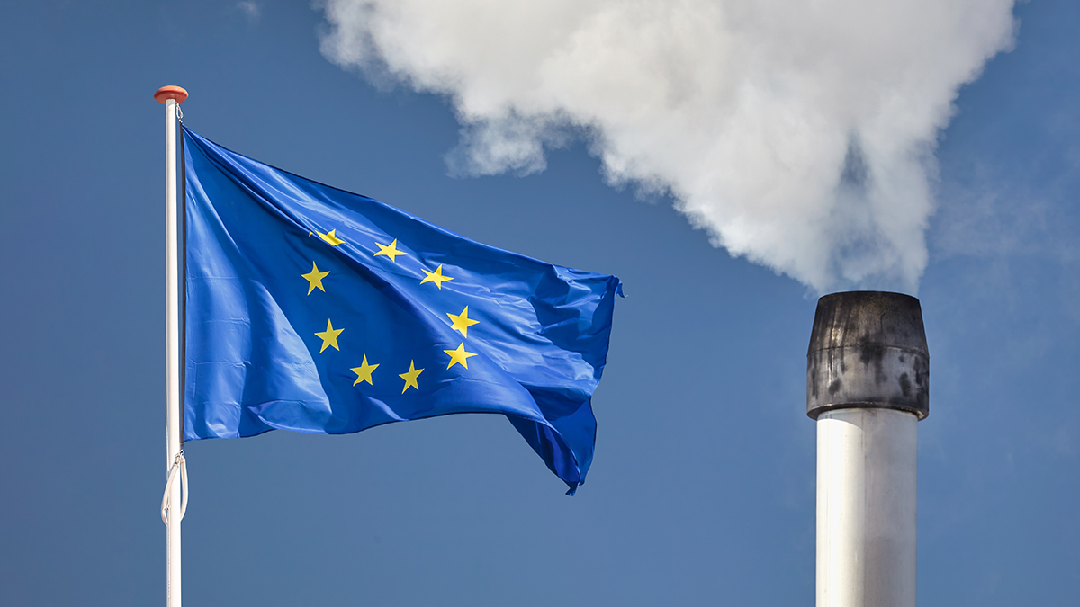 EU flag in front of a polluting factory chimney with smoke