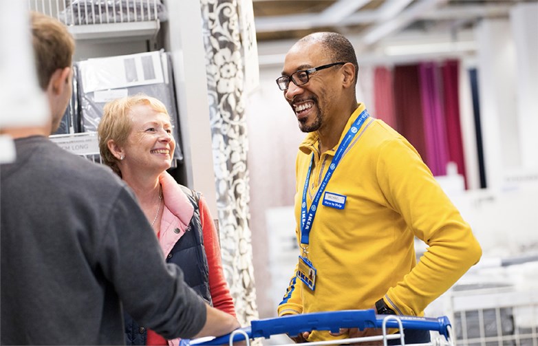 An IKEA employee talking to two customers in a store and smiling.