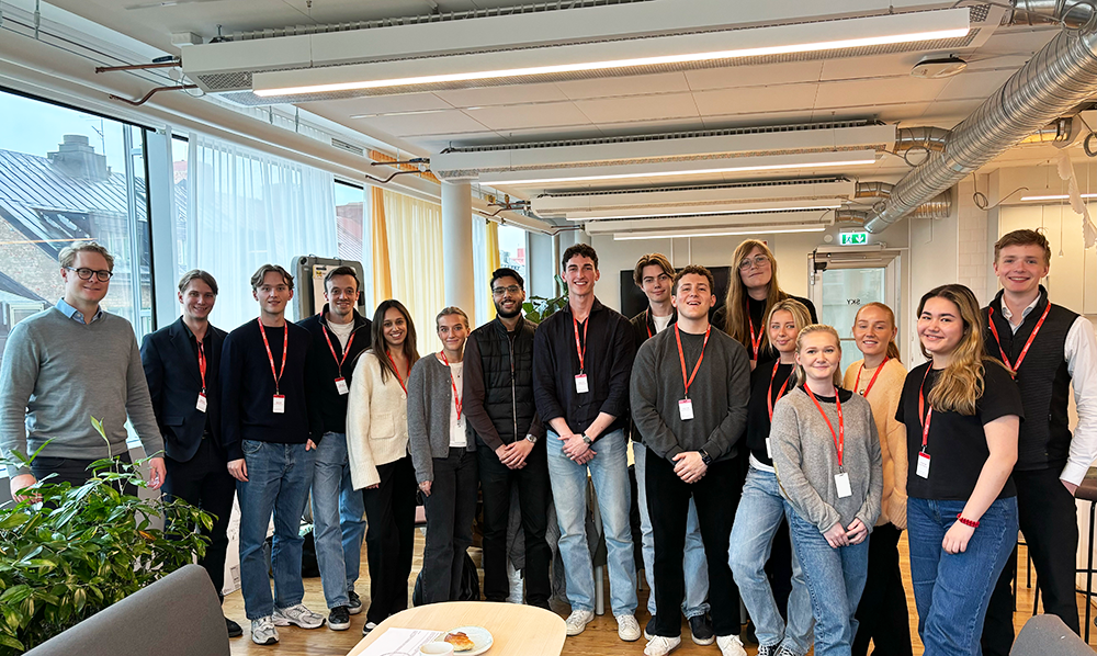 A large group of students lined up smiling in front of the camera at Accenture's HQ.