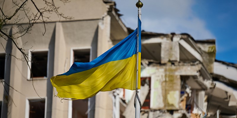 Flag of Ukraine against the background of a destroyed building in Ukraine. The building was destroyed by a Russian air bomb.