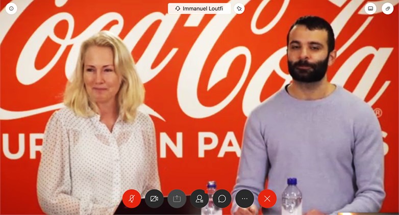 Two representatives from Coca Cola European partners, a male and female, holding a videomeeting both looking into the camara. In the background the company logo.