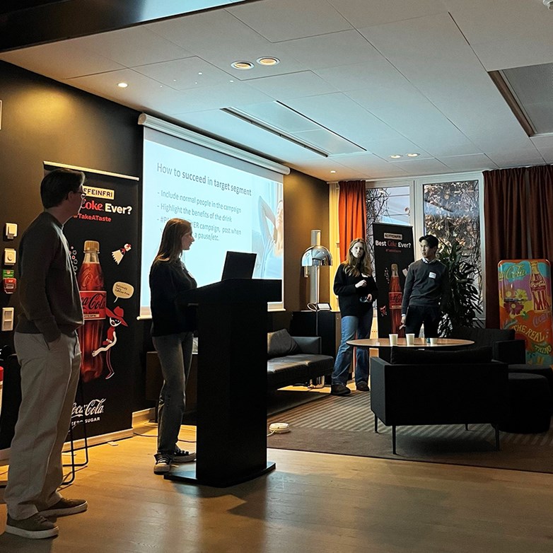 Students presenting in a dark lit conference room at Coca-Cola Europacific partners