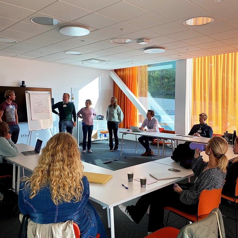 Students presenting in front of a group of people in a bright colorful conference room.
