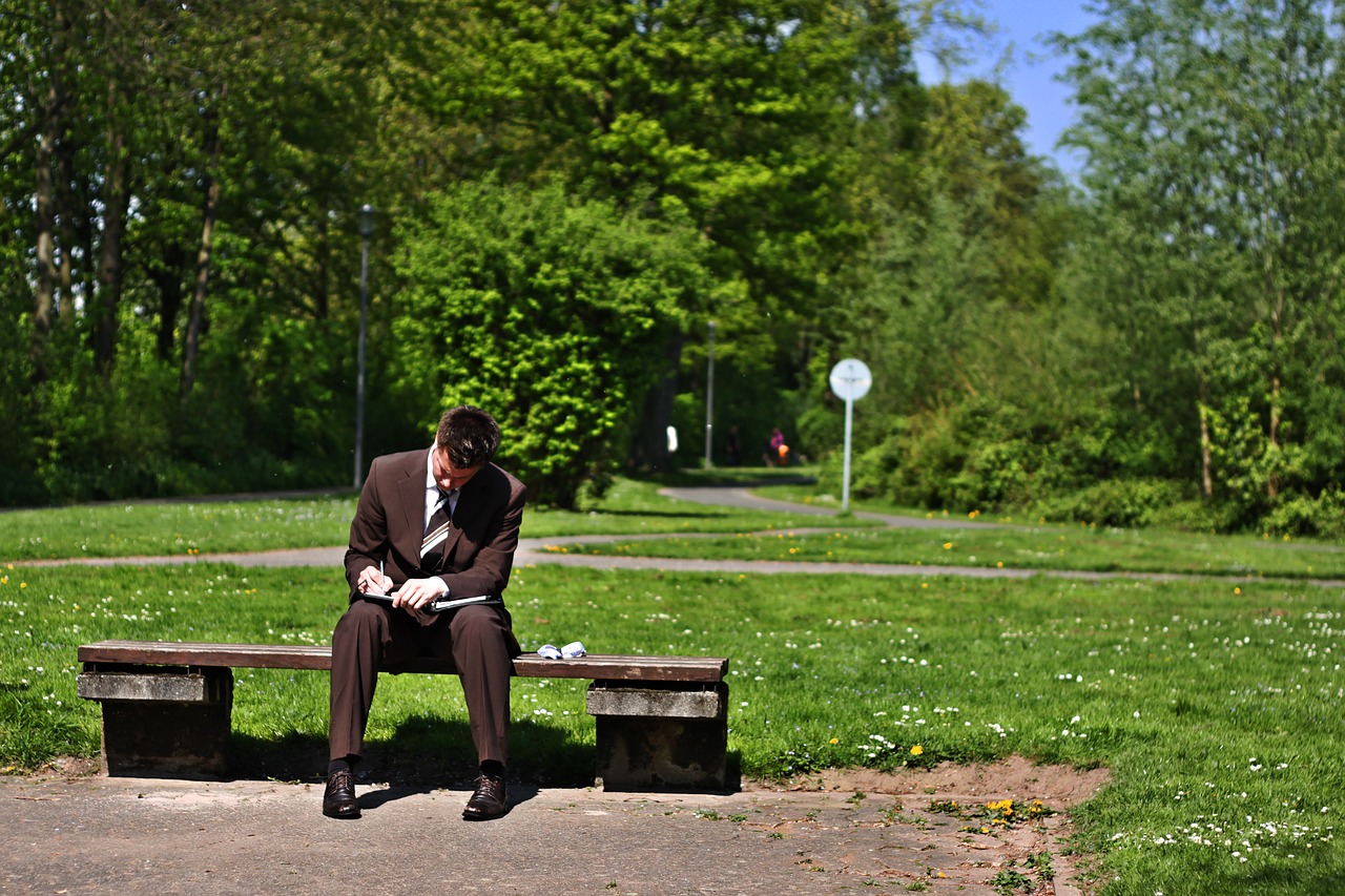 Man in business suit writing while sitting on a bench in a park