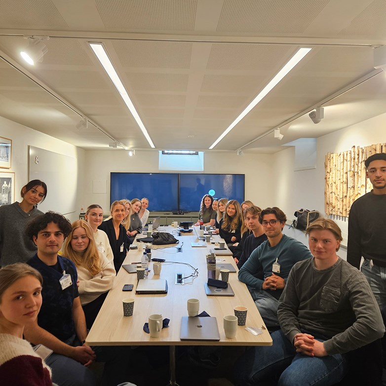 Students sitting around larger conference table looking into the camera.