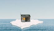 A house surrounded by melting ice. On the roof there is a signs that says "Its a hoax".