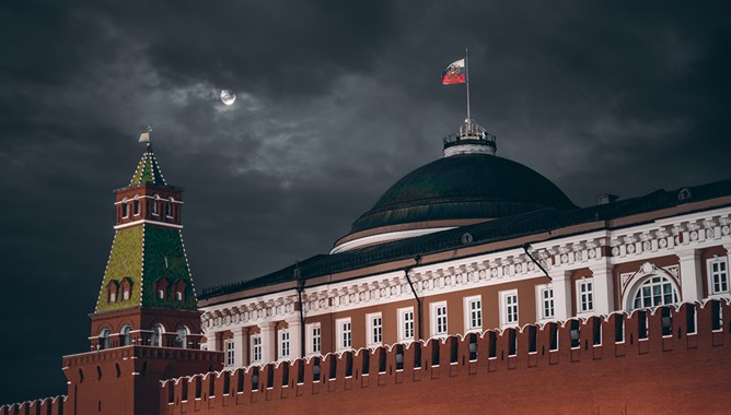 Night shot: Kremlin Moscow Dome of Senate building, a red Kremlin wall, flag of Russia with the emblem on it; sinister dark sky with a moon partly closed by the clouds.