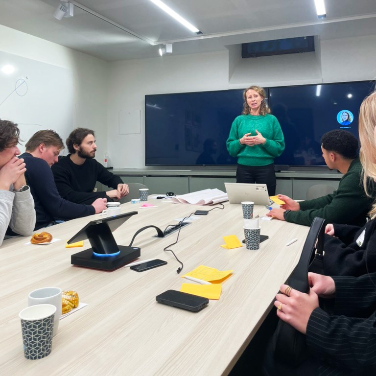 Representative from Systembolaget holds a presentation in front of students around a conference table.