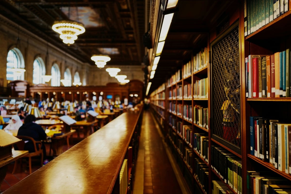 Library lined with bookshelves and books on the right-hand side and students studying at desks to the left.