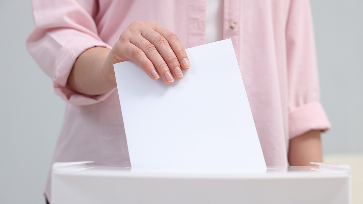 Woman putting her vote into ballot box on blurred background, closeup