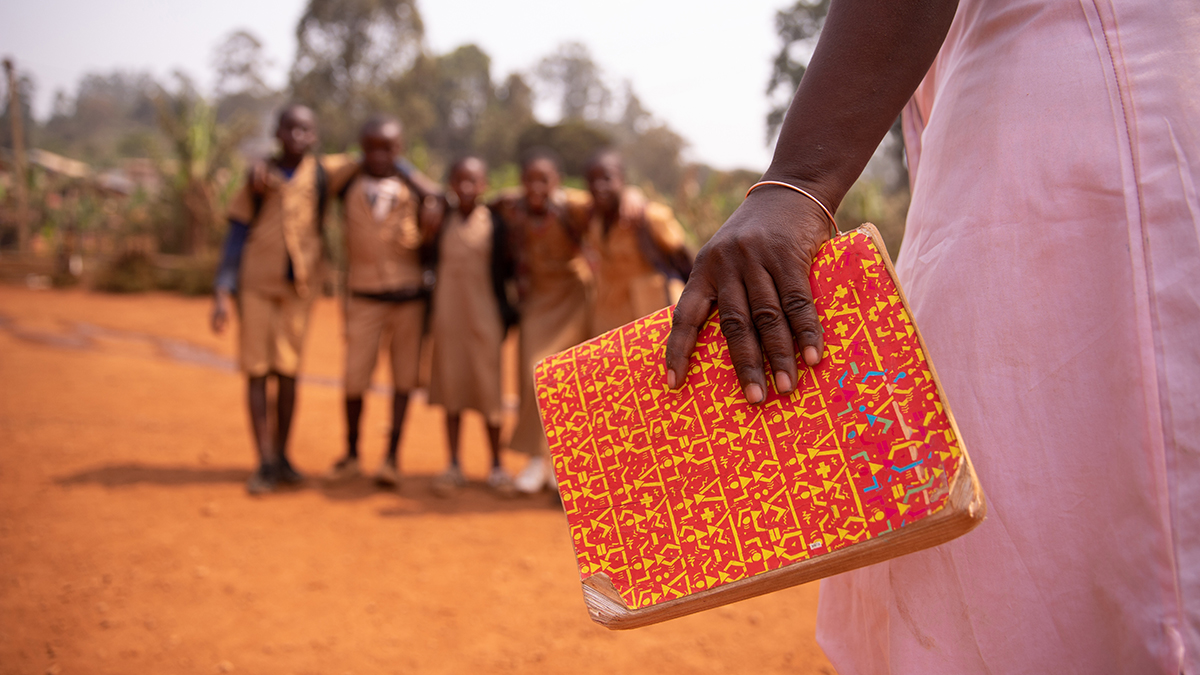 An african teacher is holding a book with her students out of focus in the background, concept of education in africa