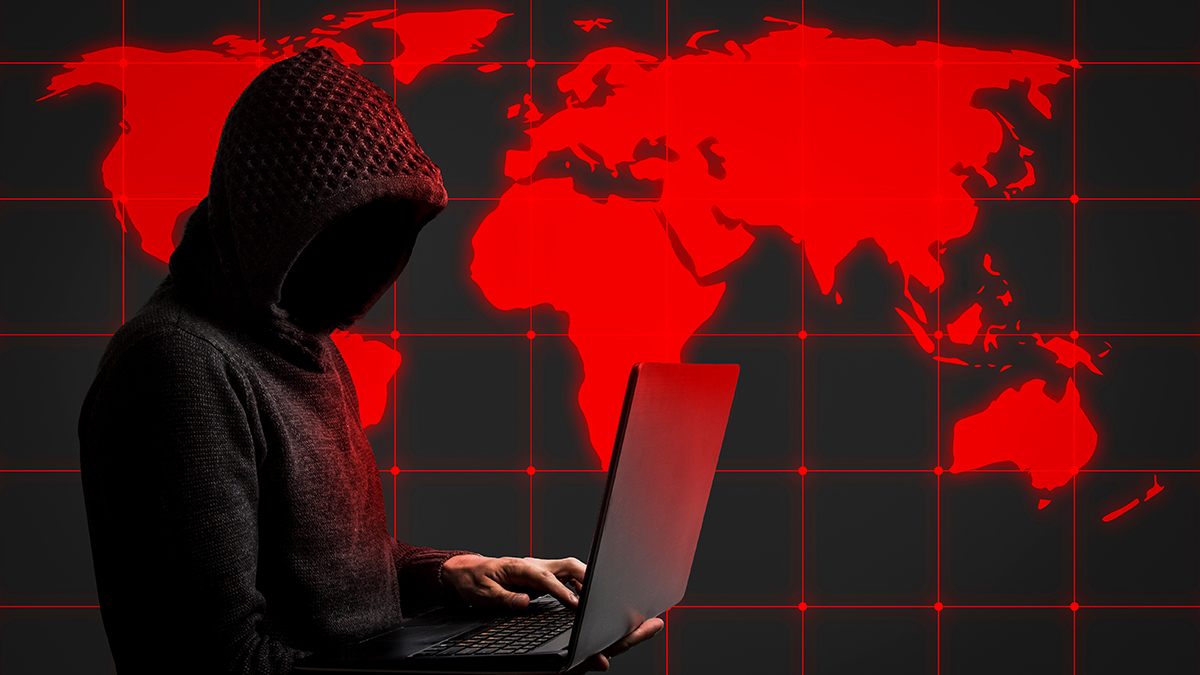 Faceless man in a hoodie with a hood holds a laptop in his hands.
