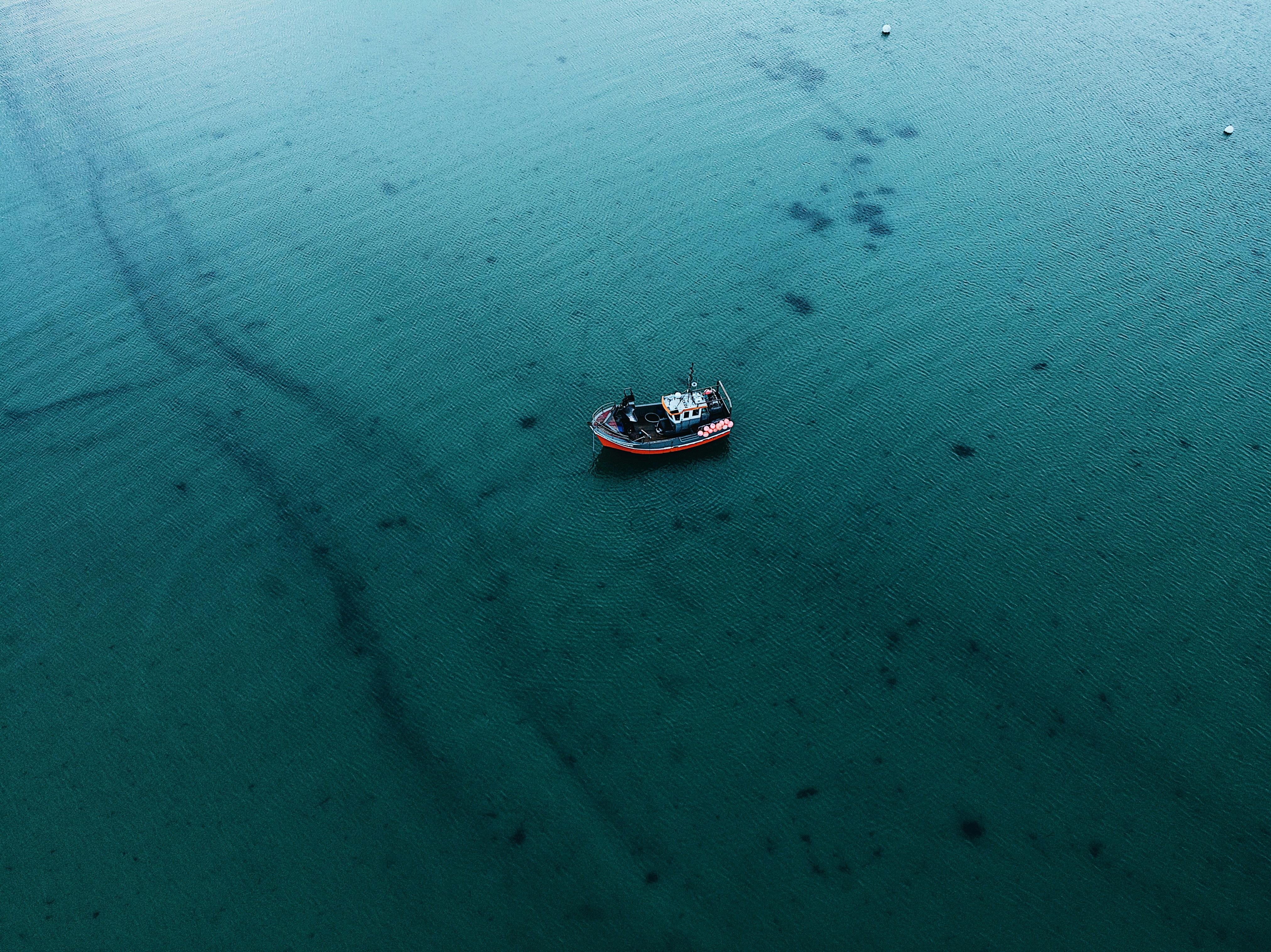 Boat floating on a blue sea streaked with an oil spill.