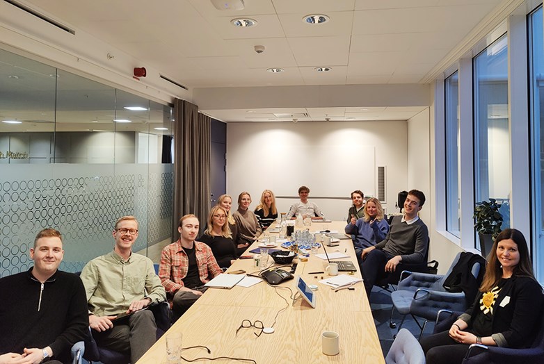 Group of students and Swedish Match representatives sitting down around a large conference table looking into the camera and smiling.
