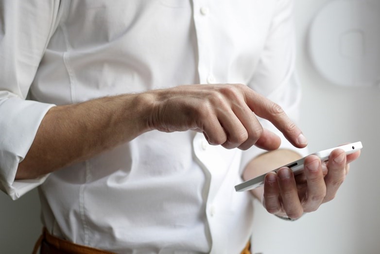 Picture of a man in white shirt cropped from the chest to the waist scrolling a smart phone.