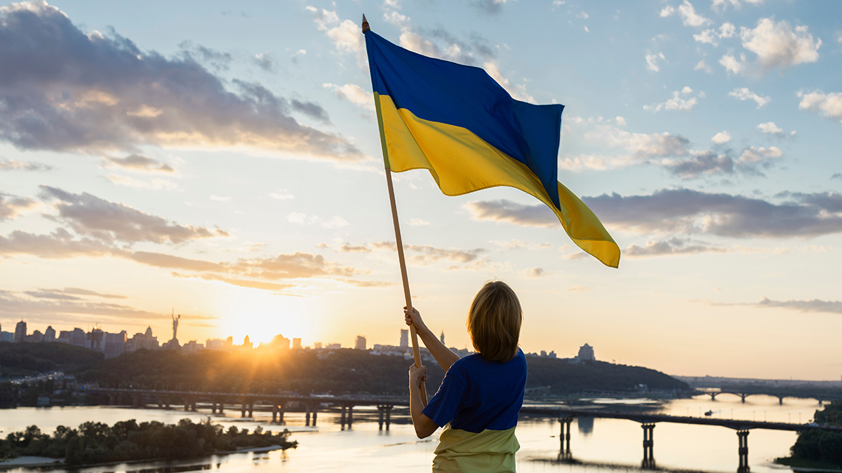 Sunset over the city of Kyiv. a woman holds a large waving Ukrainian flag standing high on the roof. Ukrainians are against war. Drawing attention to military actions in Ukraine. independence Day.