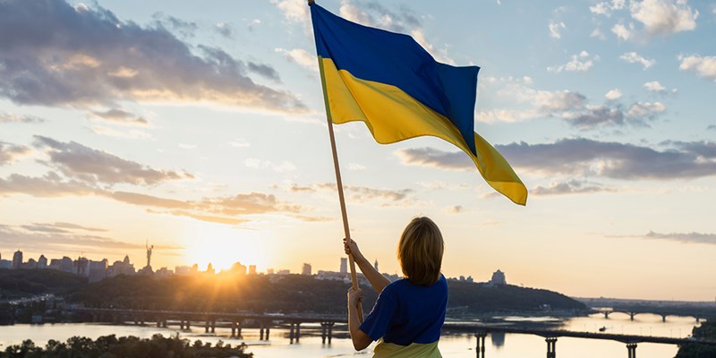 Sunset over the city of Kyiv. a woman holds a large waving Ukrainian flag standing high on the roof. Ukrainians are against war. Drawing attention to military actions in Ukraine. independence Day.