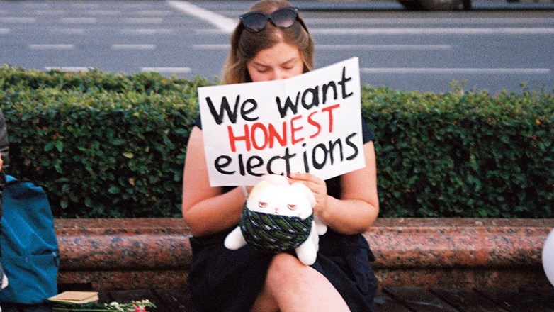 Girl sitting on a bench and holding up a protest card