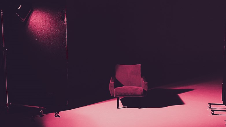 A single seated sofa in the middle of a dark room highlighted by the light of a lamp