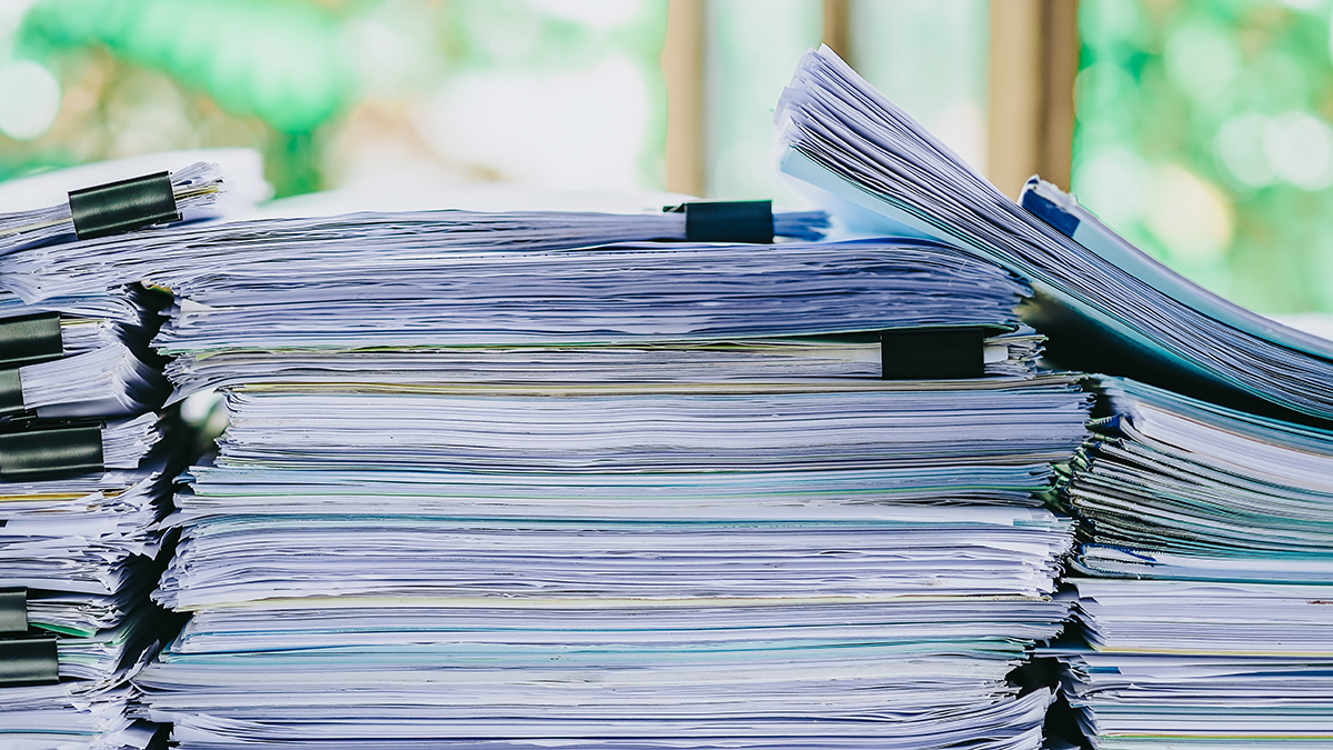 Stack of business report paper file on modern white office desk with bokeh background.
