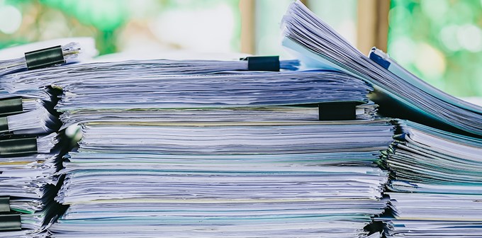 Stack of business report paper file on modern white office desk with bokeh background.