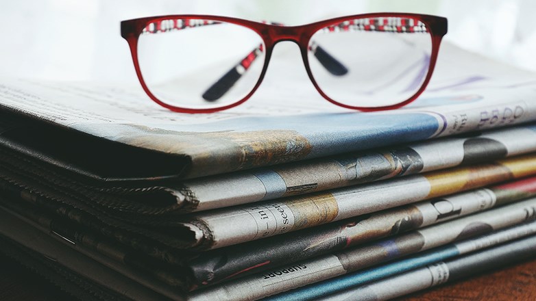 Reading glasses on top of a pile of newspapers.