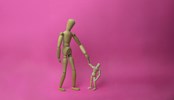 Wooden mannequin parent holding the child's hand in a pink background.