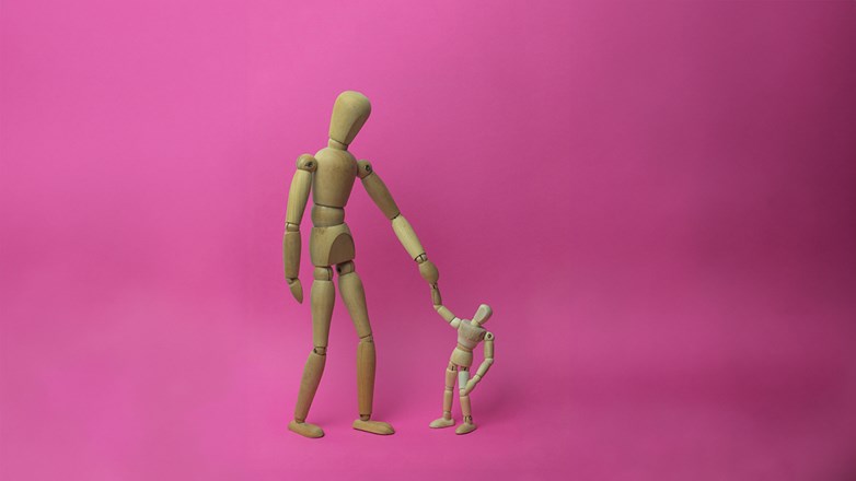 Wooden mannequin parent holding the child's hand in a pink background.