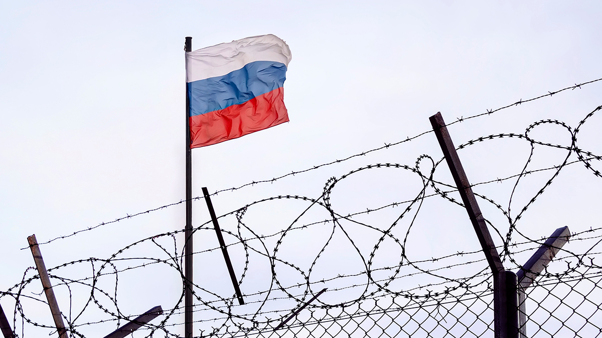 View of russian flag behind barbed wire against cloudy sky.