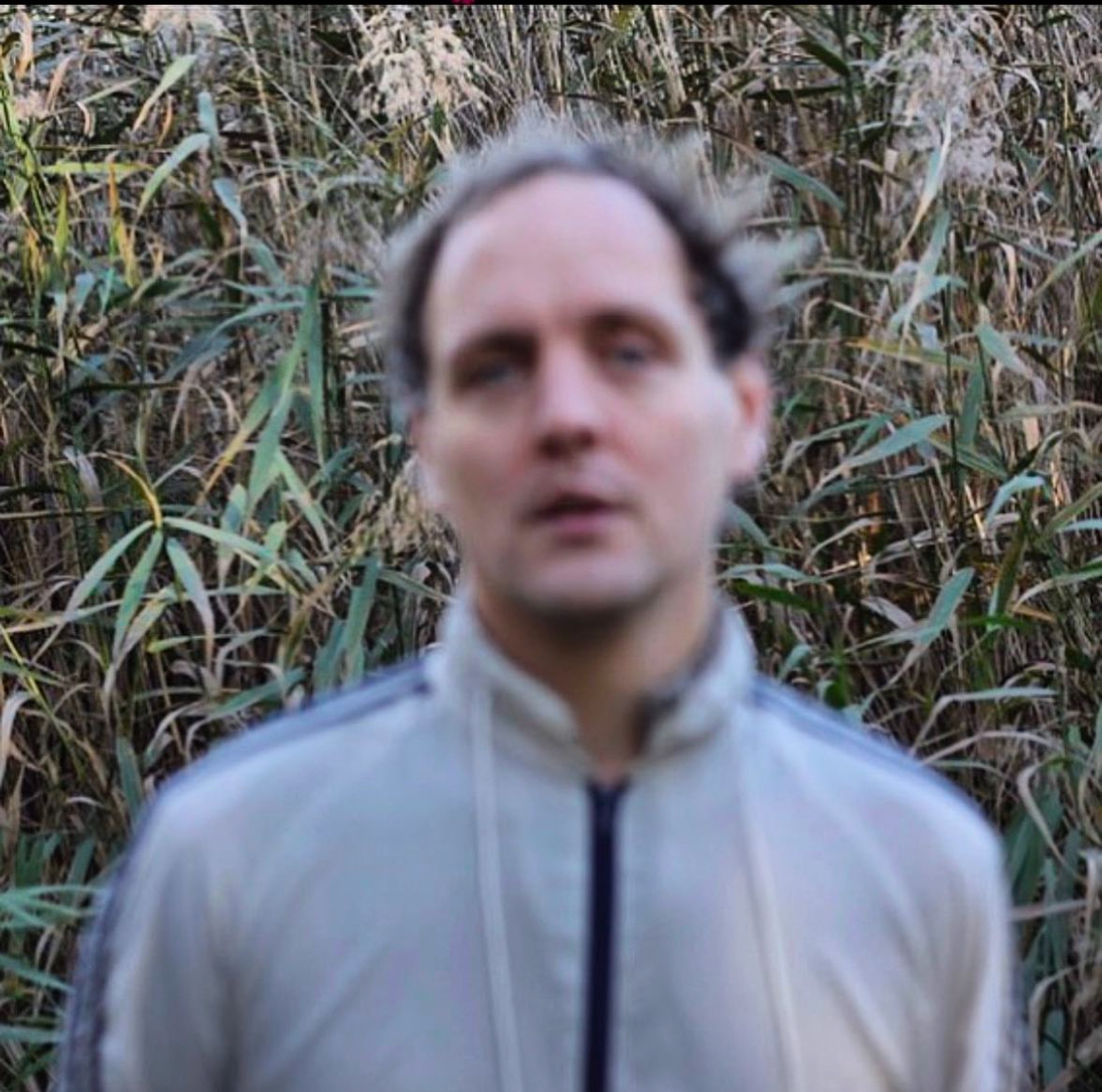 Portrait of Klas Barbrosson. Barbrosson blurred in the foreground, the background of leaves in focus.