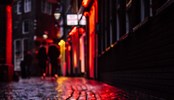 Reflection of neon lighting of showcase windows over wet pavement.
