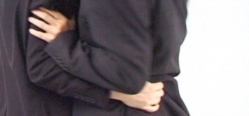 Two suited figures in black silhouette against white, cropped at neck and thigh, caught mid-movement.