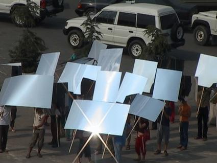 Still from Mircea Cantor's film The Landscape is Changing, showing marchers with mirrored placards in Tirana