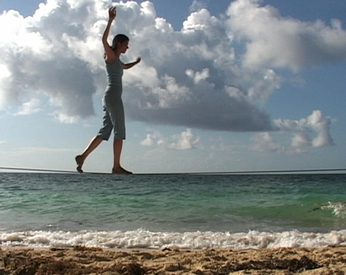 Still from Janine Antoni's video Touch, showing the artist walking a tightrope along a beach horizon